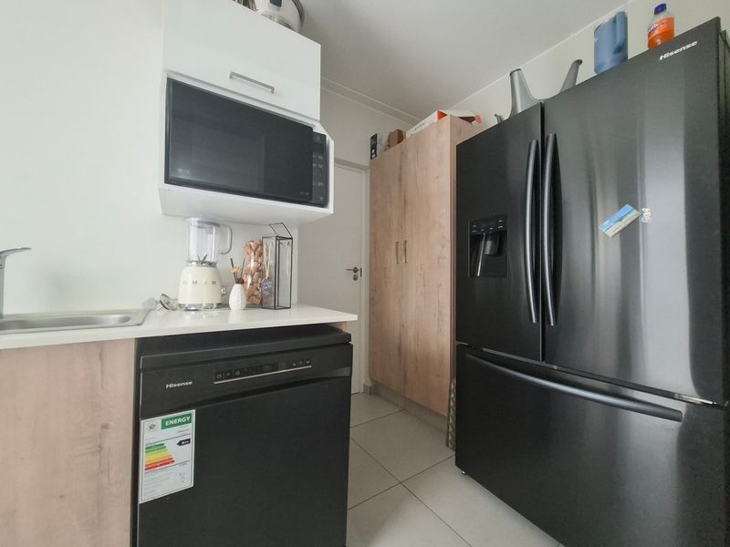 A compact kitchen featuring modern wood-finish cabinetry, a built-in microwave, integrated dishwasher, and tiled flooring, providing a functional and efficient workspace.