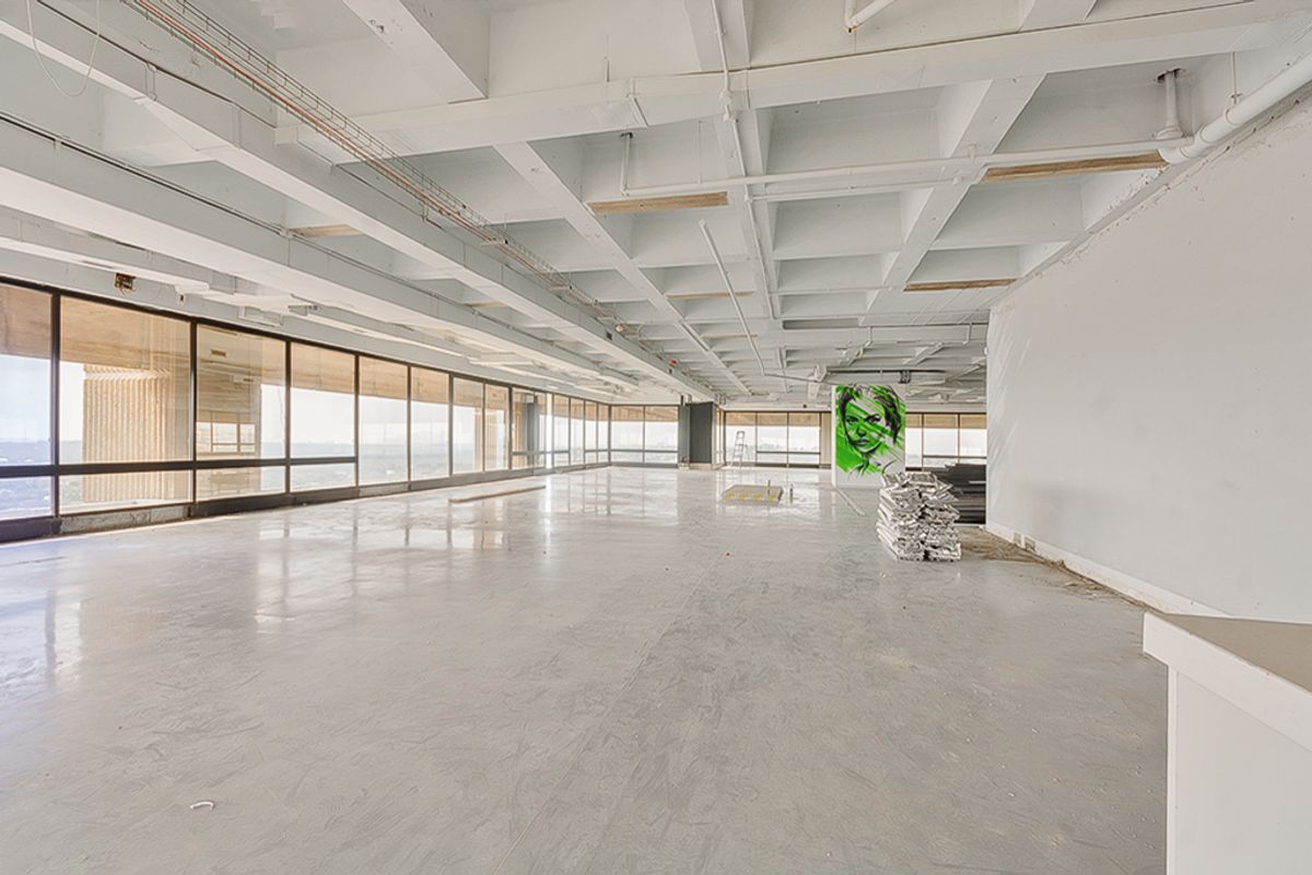 Expansive open-plan commercial office space featuring high exposed waffle ceilings, polished concrete floors, and extensive floor-to-ceiling windows offering panoramic views.