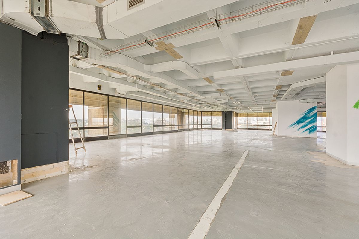 Expansive open-plan commercial office space featuring polished concrete floors, exposed industrial ceiling, and floor-to-ceiling windows offering extensive natural light and city views.