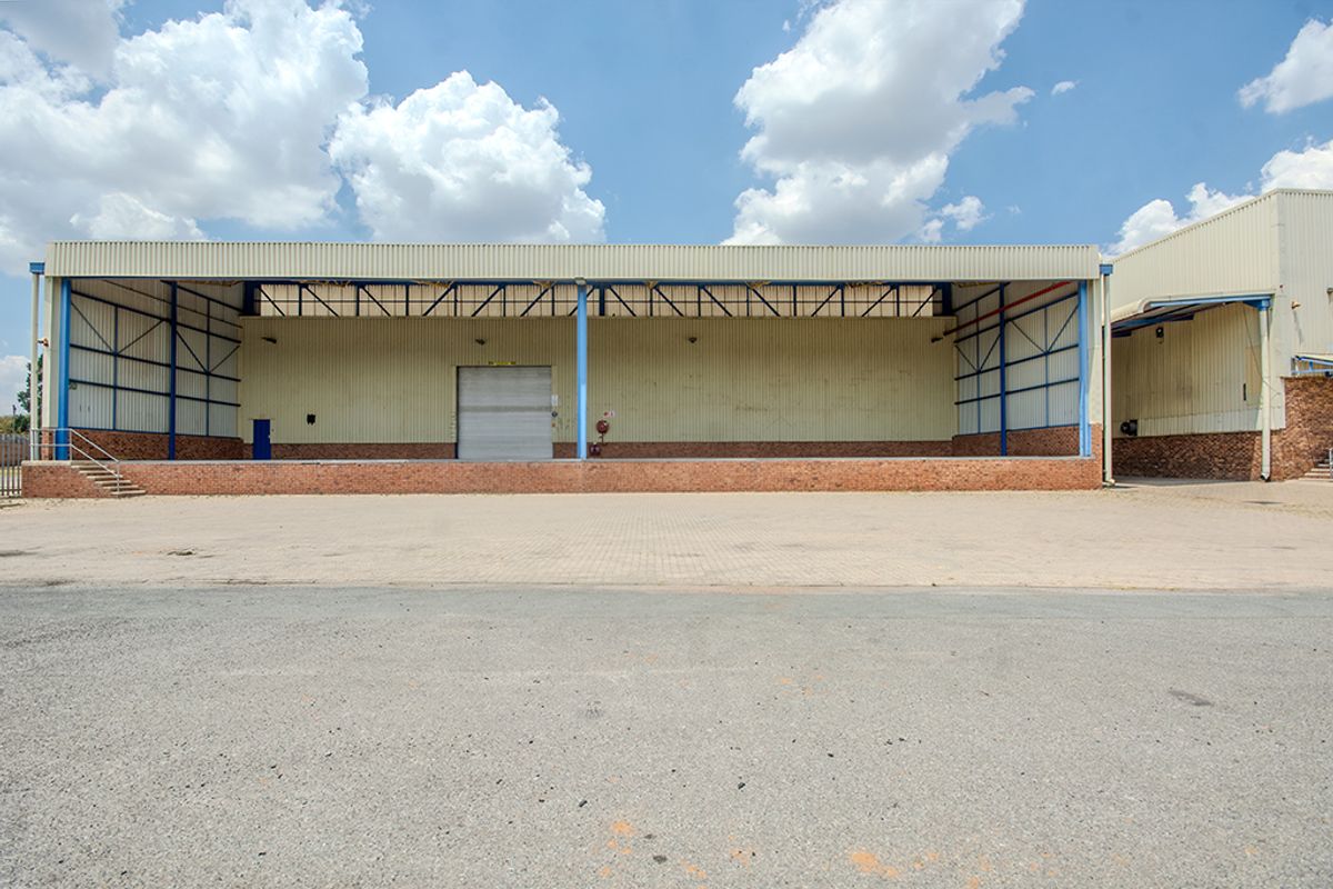 Industrial warehouse exterior featuring a large raised loading dock, roller shutter door, and durable steel portal frame construction with a paved yard.
