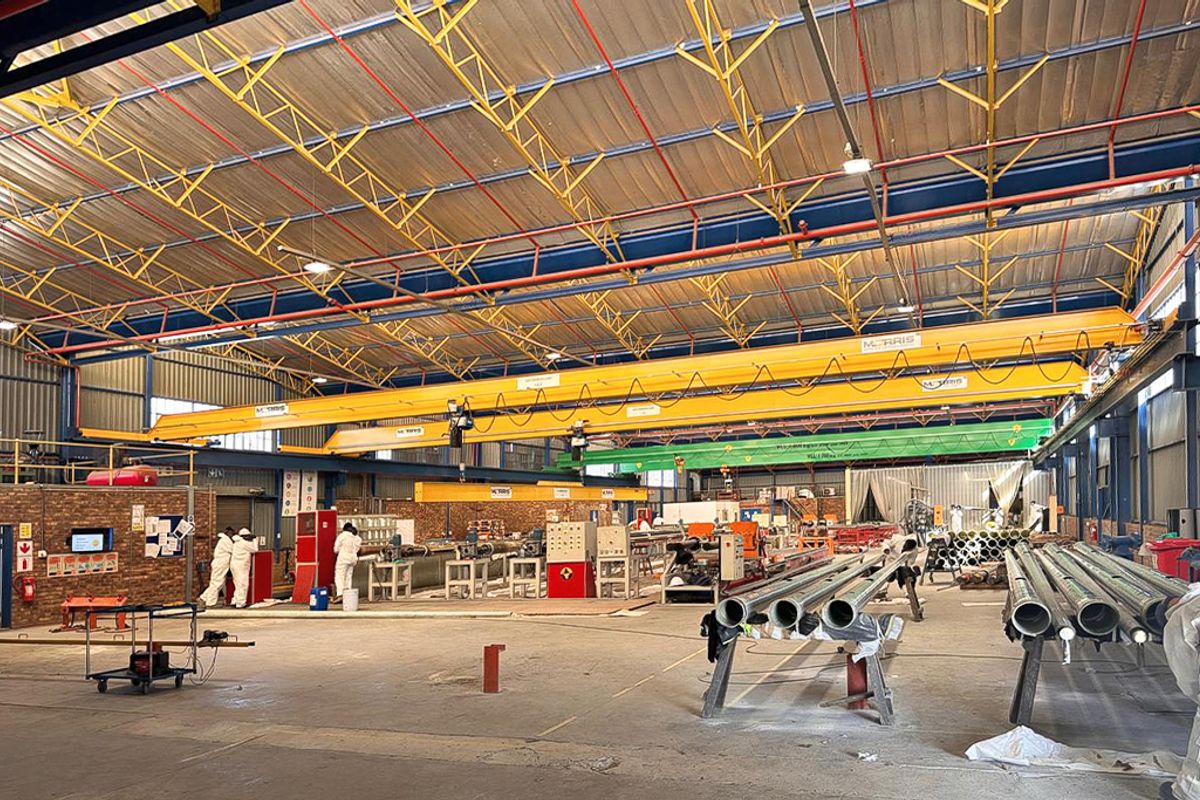 Spacious industrial warehouse facility featuring high ceilings with exposed steel trusses, multiple overhead bridge cranes, and durable concrete flooring.