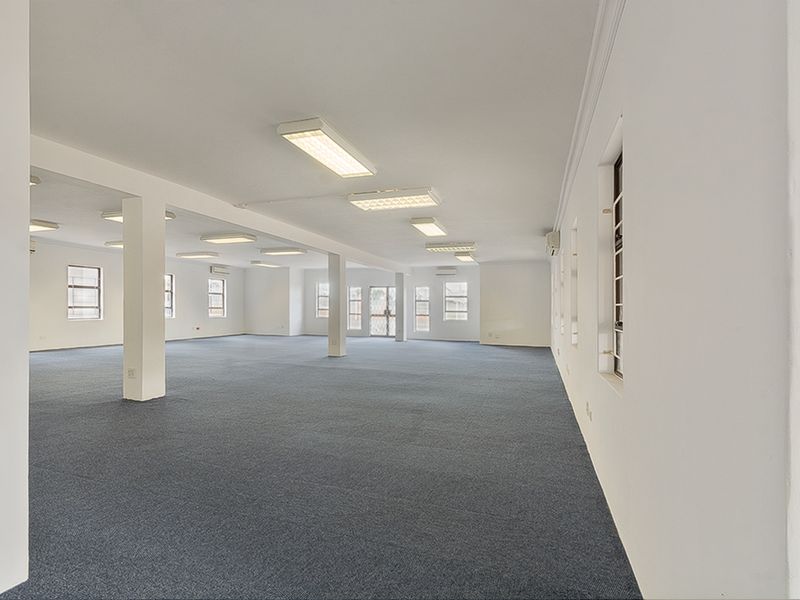 Spacious, open-plan commercial office area featuring neutral finishes, carpeted flooring, ample natural light, and integrated air conditioning units.
