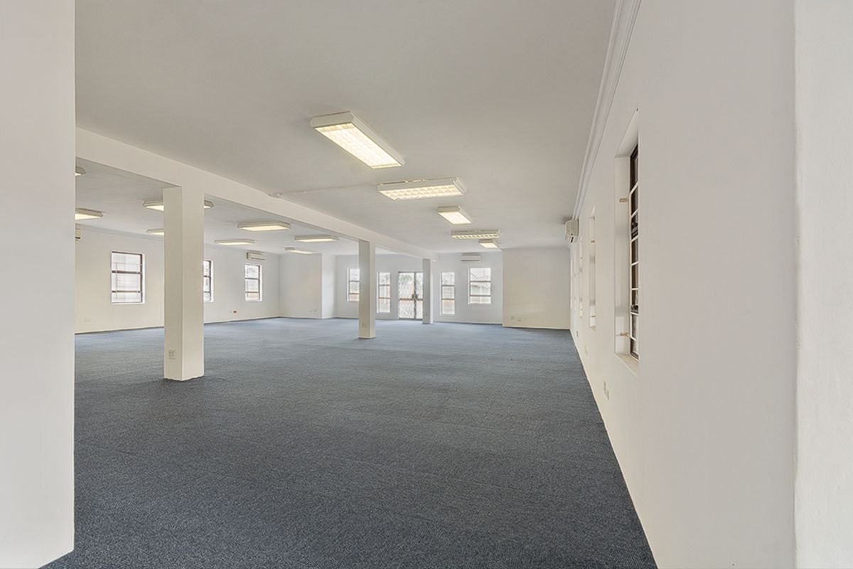 Spacious, open-plan commercial office area featuring neutral finishes, carpeted flooring, ample natural light, and integrated air conditioning units.