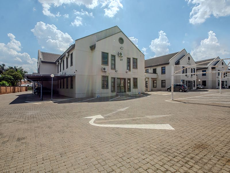 Exterior view of a commercial office complex featuring a paved parking lot, covered parking bays, and multi-story building facades.