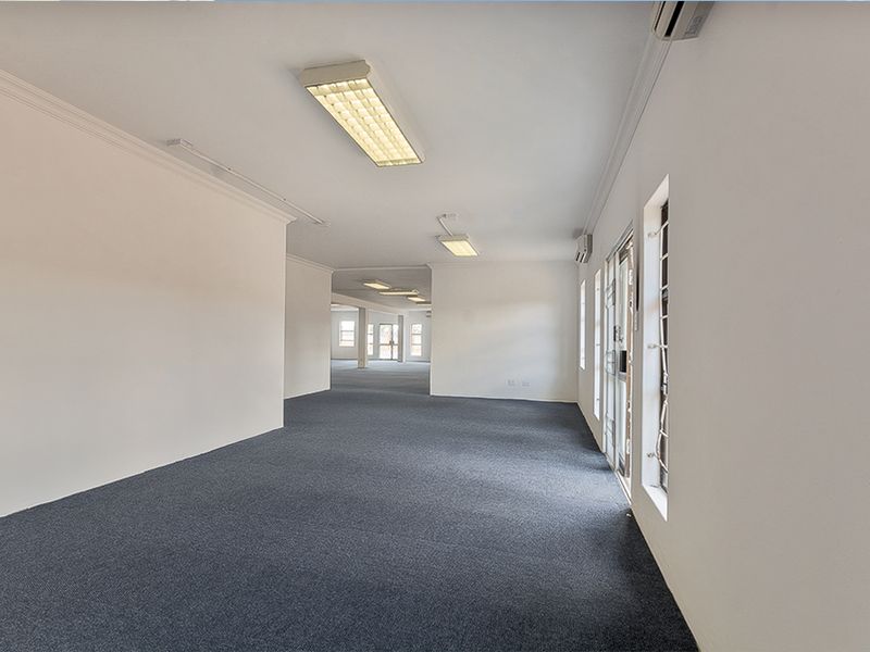 Spacious, open-plan commercial office area featuring neutral walls, carpeted flooring, and integrated fluorescent lighting with air conditioning units.