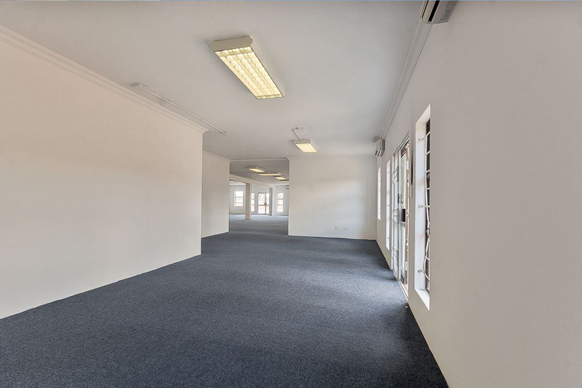 Spacious, open-plan commercial office area featuring neutral walls, carpeted flooring, and integrated fluorescent lighting with air conditioning units.