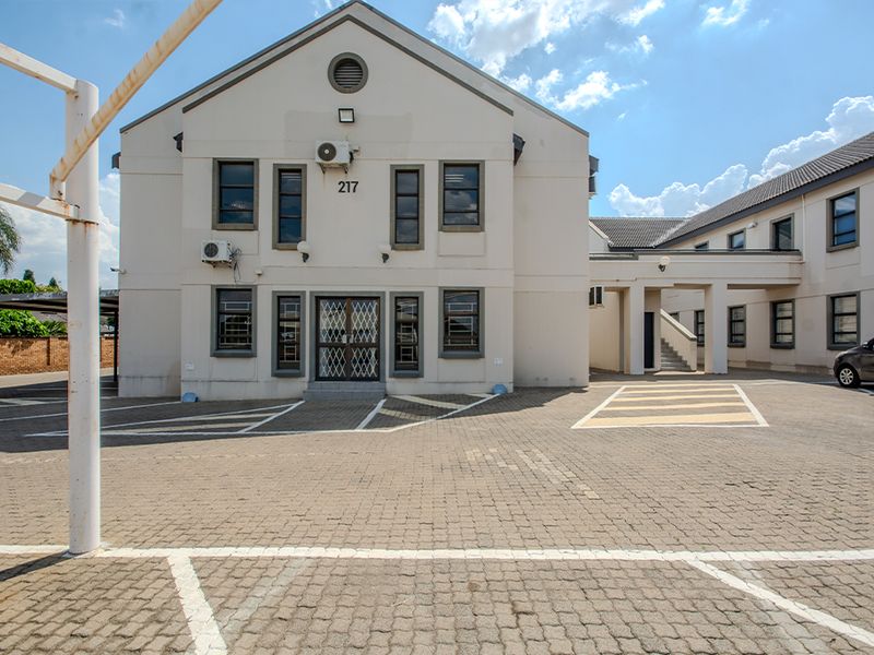 Front elevation of a commercial building featuring a paved parking area, security gate, and covered walkway access.