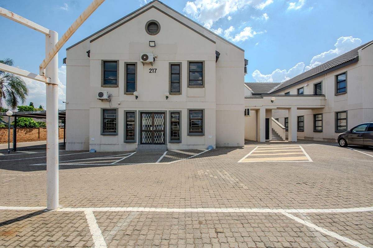 Front elevation of a commercial building featuring a paved parking area, security gate, and covered walkway access.