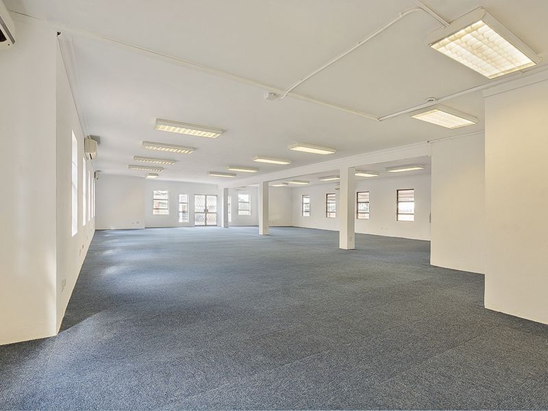 A spacious, open-plan commercial office area featuring neutral finishes, carpeted flooring, and overhead fluorescent lighting, suitable for a variety of business configurations.
