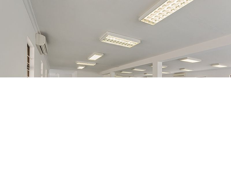 A bright, open-plan commercial office space featuring recessed fluorescent lighting and wall-mounted air conditioning units.