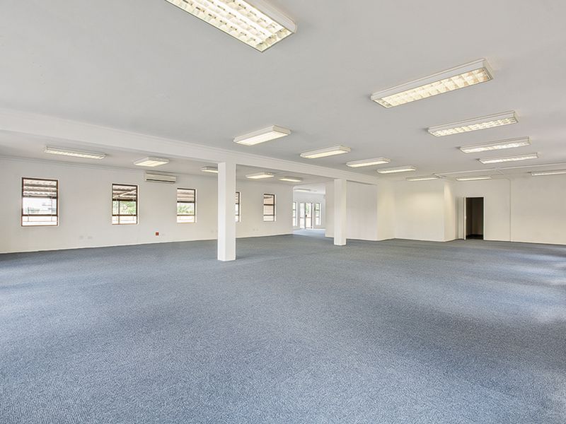 A spacious, open-plan commercial office area featuring neutral carpeting, multiple support columns, and integrated fluorescent lighting throughout.