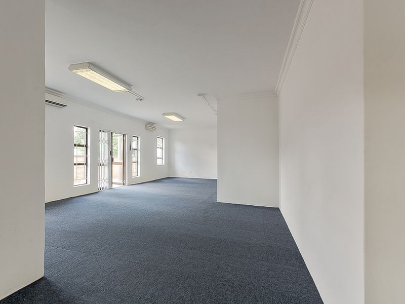 A spacious, empty commercial office area featuring neutral walls, carpeted flooring, integrated fluorescent lighting, and split-system air conditioning units.