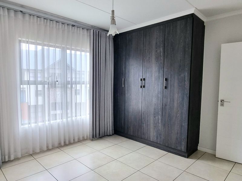 A bright, empty bedroom featuring neutral tiled flooring and dark wood-grain built-in cupboards, offering a clean and versatile space.