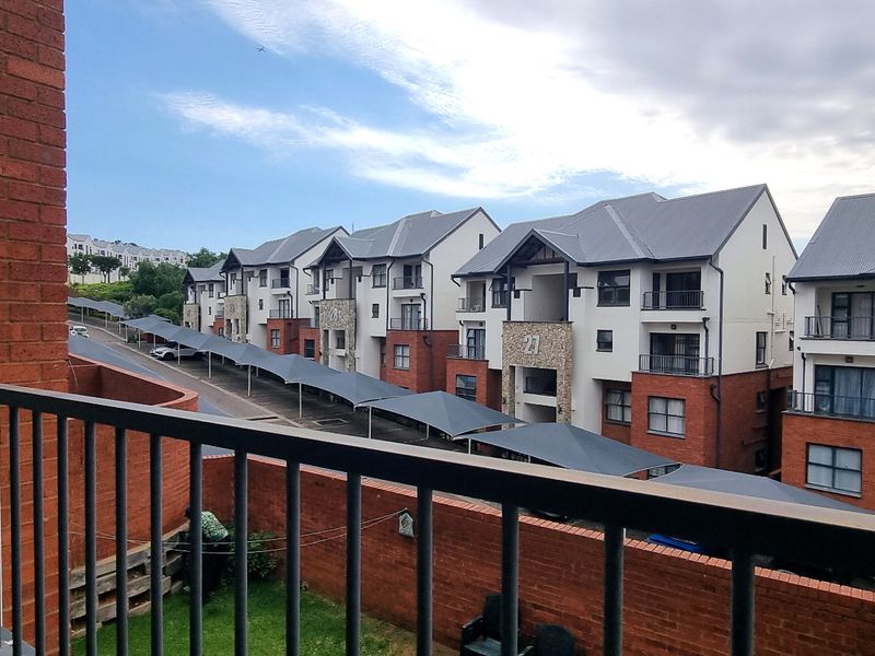 An elevated view from a balcony overlooking the townhouse complex, featuring brick architecture, metal balustrades, and covered parking bays.