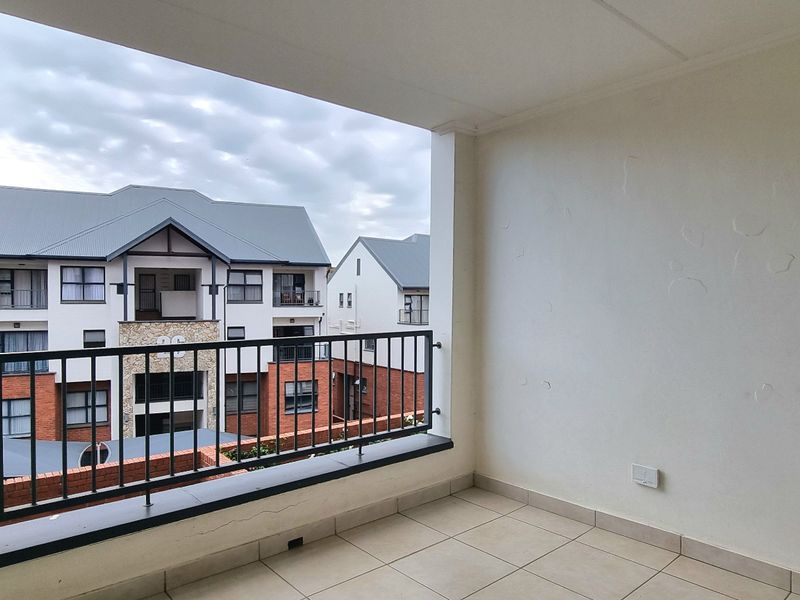A covered balcony featuring tiled flooring and a metal balustrade, offering an open view of the surrounding townhouse complex.