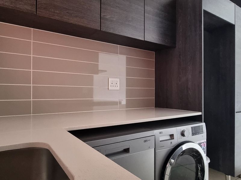 Modern laundry area featuring sleek dark cabinetry, stone countertops, tiled backsplash, and dedicated spaces for integrated appliances.
