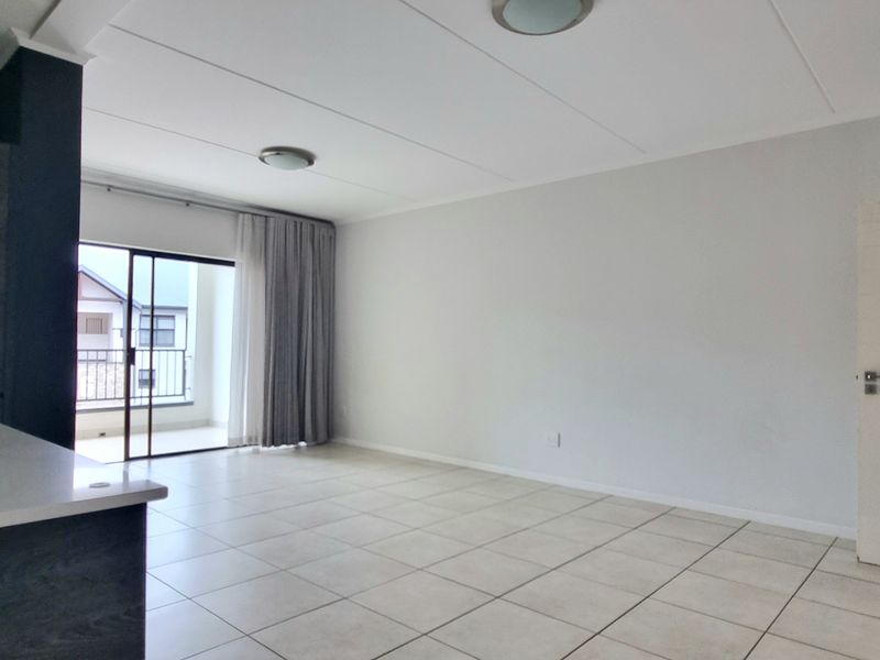 Spacious open-plan living area featuring neutral tiled flooring, modern cabinetry, and a sliding glass door leading to an outdoor balcony.