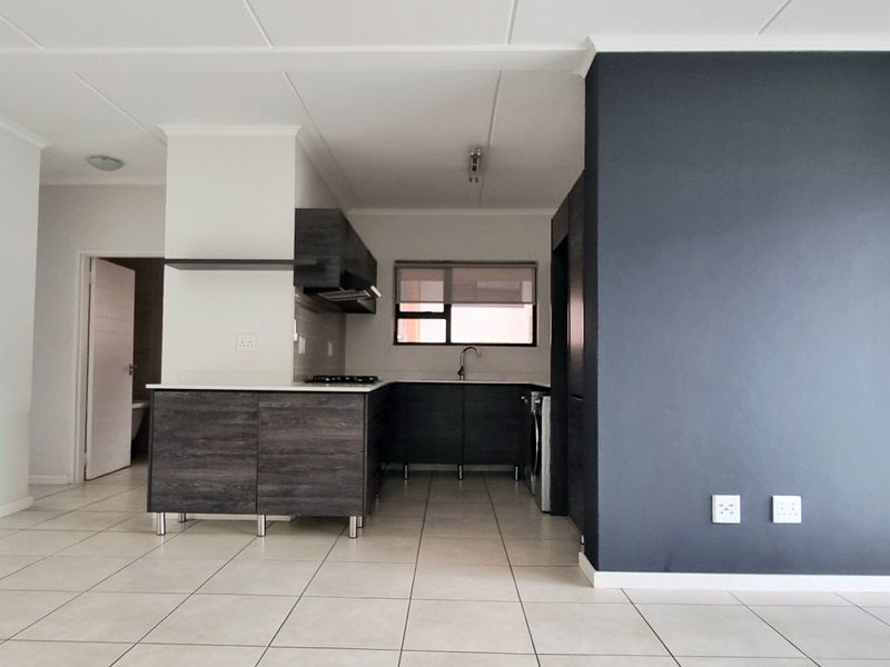 Spacious open-plan living and kitchen area featuring modern dark cabinetry, a gas hob, tiled flooring, and a striking dark accent wall.