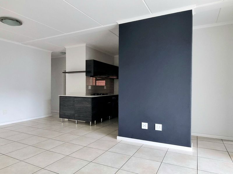 Spacious open-plan living area featuring neutral tiled flooring, a modern dark-toned kitchen, and a large sliding door providing access to the exterior.