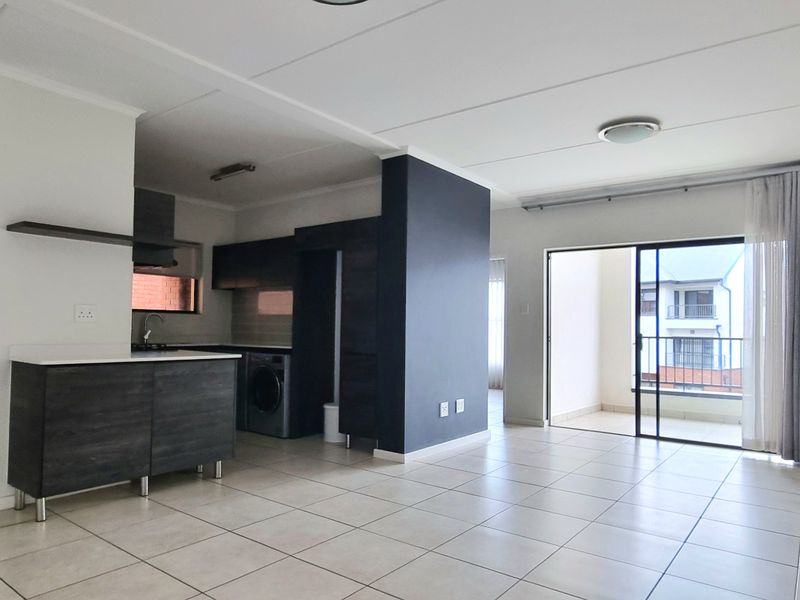 Spacious open-plan living area featuring tiled floors, modern kitchen cabinetry, and direct access to a private balcony through large sliding glass doors.