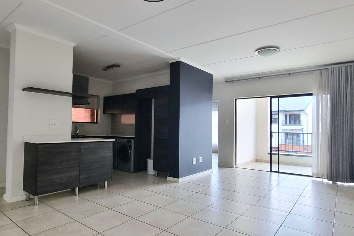 Spacious open-plan living area featuring tiled floors, modern kitchen cabinetry, and direct access to a private balcony through large sliding glass doors.