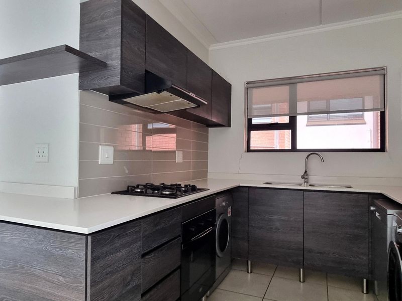 Modern kitchen featuring dark wood cabinetry, stone countertops, gas hob, built-in oven, and integrated laundry appliance space.