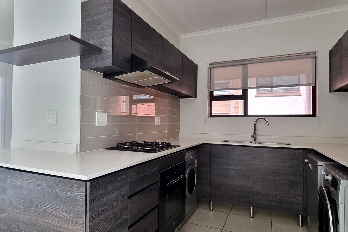 Modern kitchen featuring dark wood cabinetry, stone countertops, gas hob, built-in oven, and integrated laundry appliance space.