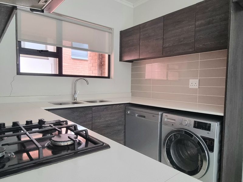 Modern kitchen featuring dark wood cabinetry, stone countertops, gas hob, extractor fan, and integrated space for laundry appliances with a tiled splashback.