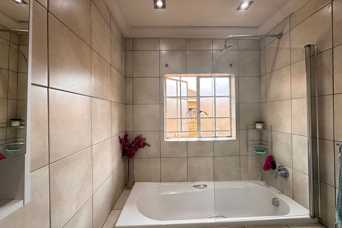 A well-maintained bathroom featuring a built-in bathtub with a glass shower screen, neutral ceramic wall tiling, and recessed ceiling lighting.