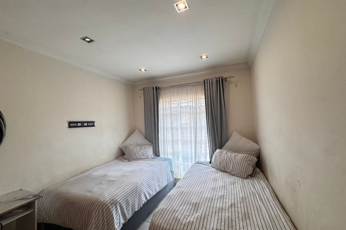 A compact bedroom featuring tiled flooring, recessed ceiling lighting, and a wall-mounted TV bracket, providing a functional space with neutral finishes.