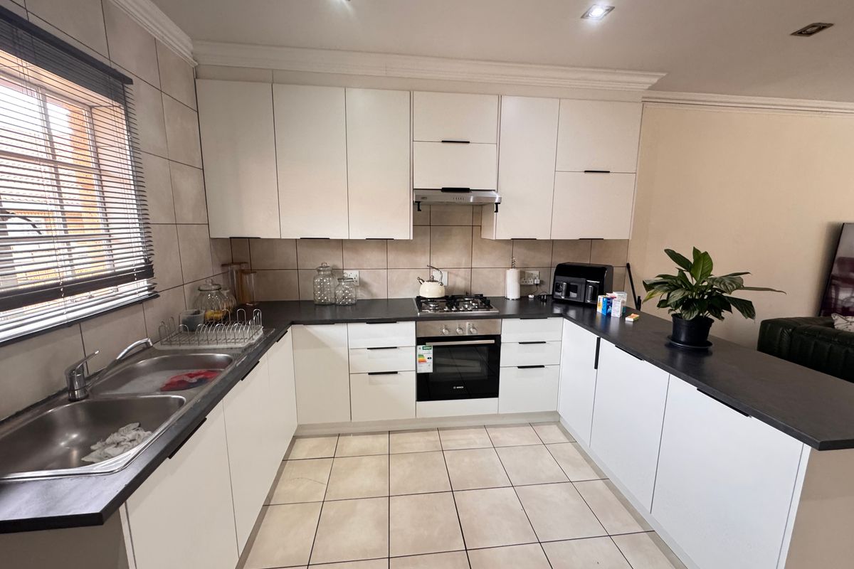 Modern kitchen featuring white cabinetry, dark countertops, gas hob, electric oven, and a functional breakfast bar layout with tiled flooring.