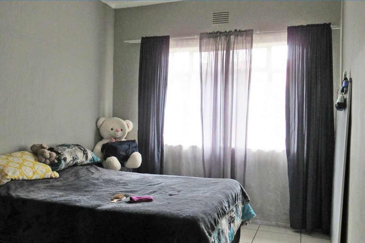A standard bedroom featuring tiled flooring, a window with curtain fixtures, and a wall-mounted ventilation grille.
