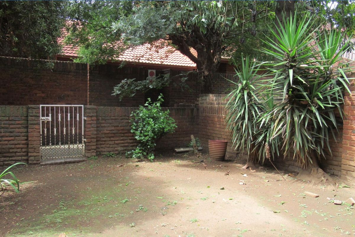A private rear courtyard area featuring brick boundary walls, a metal security gate, and established garden vegetation.