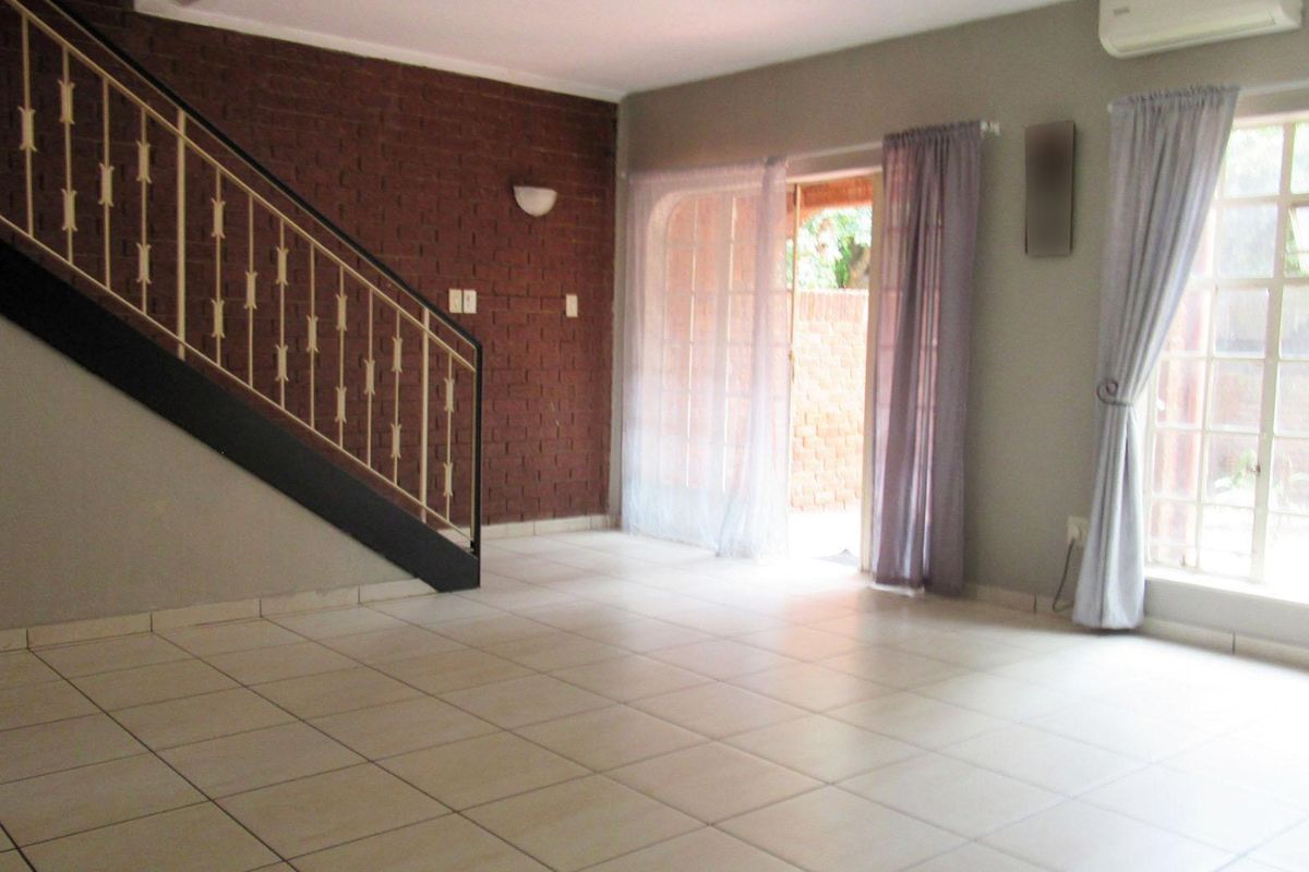 Spacious living area featuring tiled flooring, an exposed brick feature wall, a staircase, and direct access to an outdoor patio area.