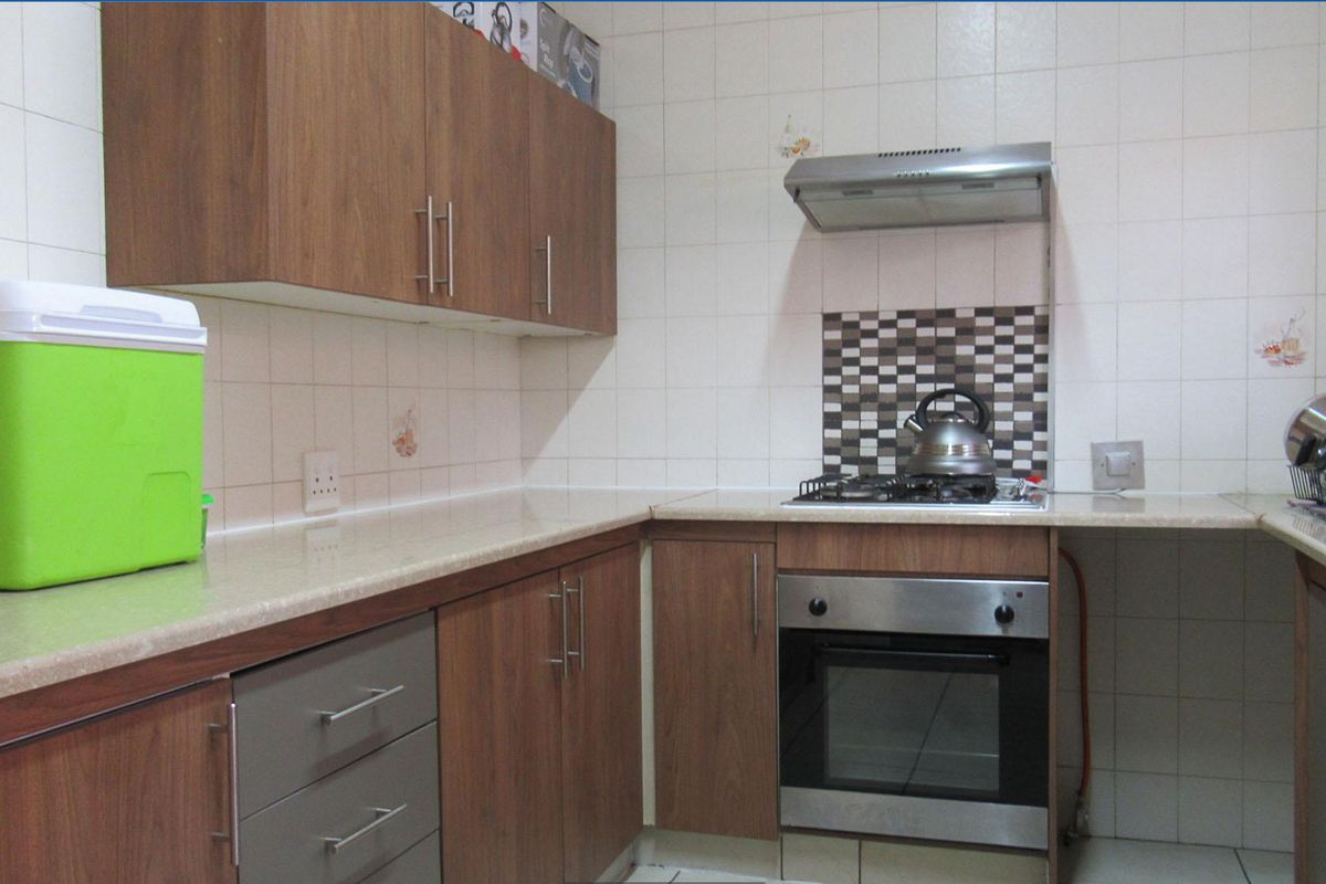 Functional kitchen featuring wood-finish cabinetry, laminate countertops, built-in oven, gas hob, and tiled splashback.