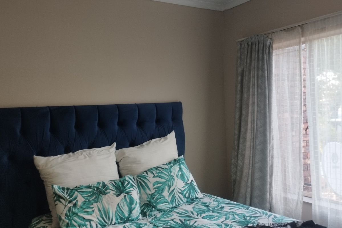 A bedroom featuring neutral wall tones and a window with installed curtain tracks, providing natural light to the space.