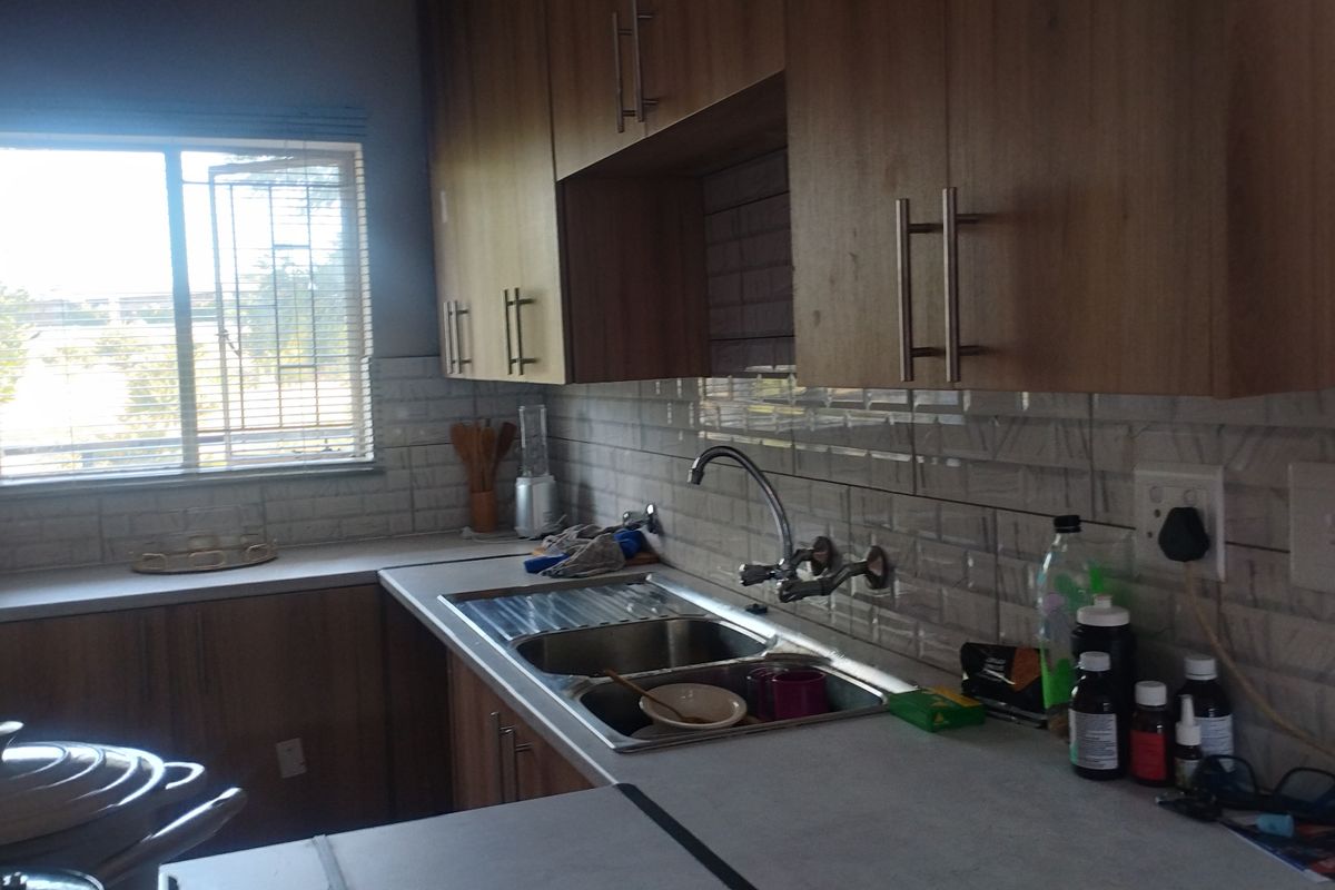 Functional kitchen featuring wood-look cabinetry, subway tile backsplash, stainless steel double sink, and ample countertop space with natural light from the window.