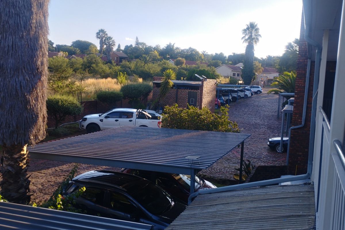 View from an elevated balcony overlooking a paved parking area with carports and surrounding residential landscaping.
