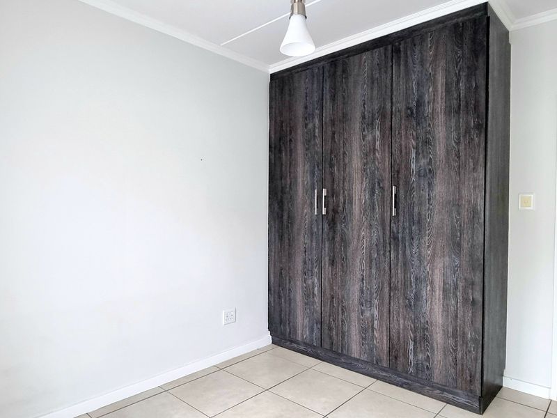 A clean, empty bedroom featuring modern dark wood-grain built-in cupboards, neutral tiled flooring, and crisp white walls.