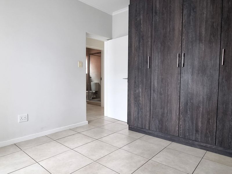 A clean, empty bedroom featuring modern dark wood-grain built-in cupboards, neutral tiled flooring, and direct access to an en-suite bathroom.