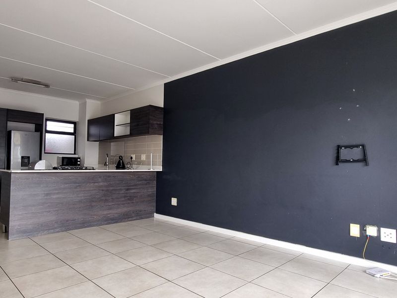 Open-plan living area featuring a modern kitchen with dark cabinetry, a breakfast island, and neutral tiled flooring throughout.