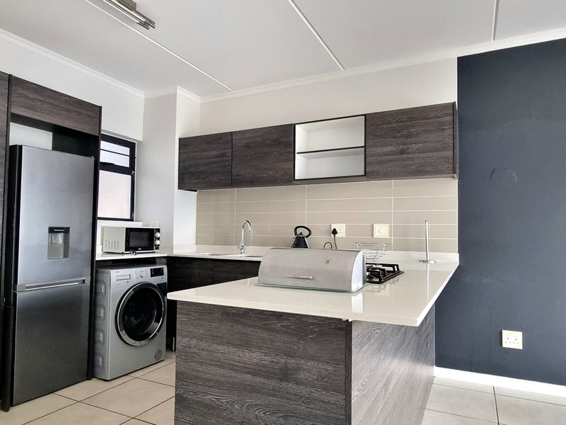 Modern kitchen featuring dark wood-grain cabinetry, stone countertops, a gas hob, and integrated space for appliances, finished with neutral tiled flooring.