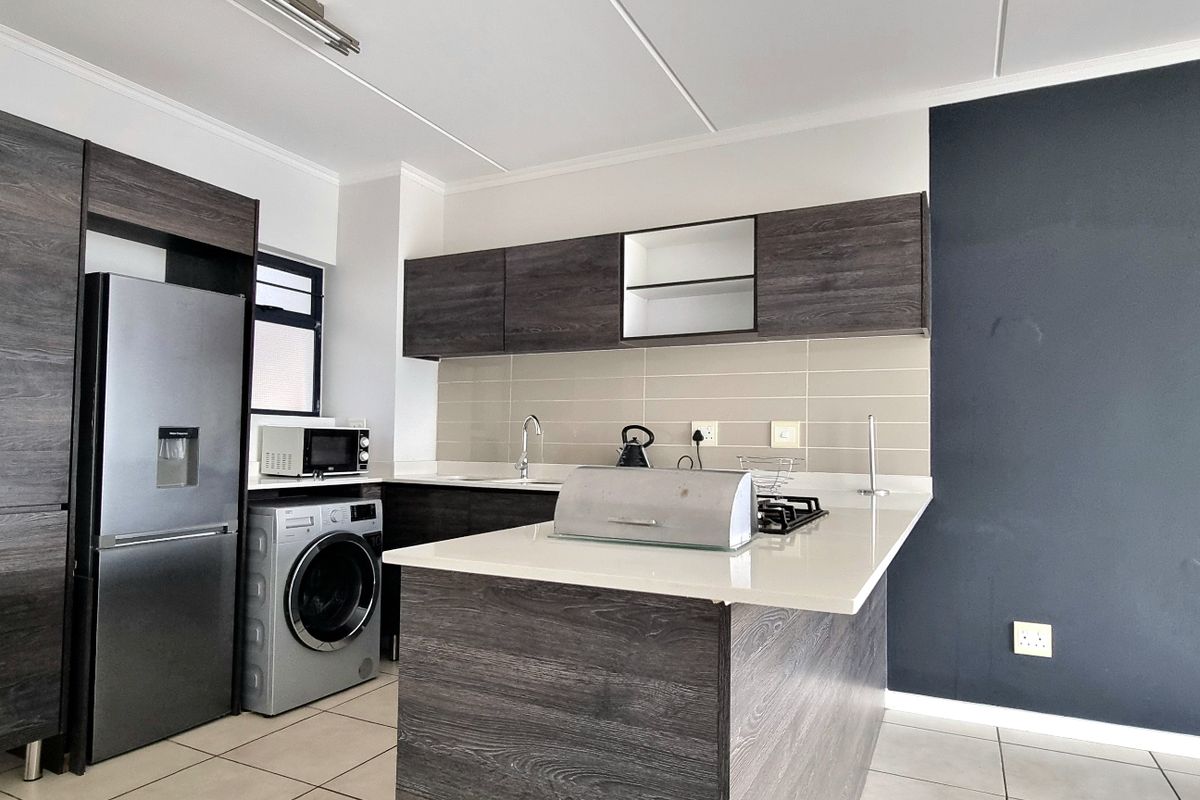 Modern kitchen featuring dark wood-grain cabinetry, stone countertops, a gas hob, and integrated space for appliances, finished with neutral tiled flooring.