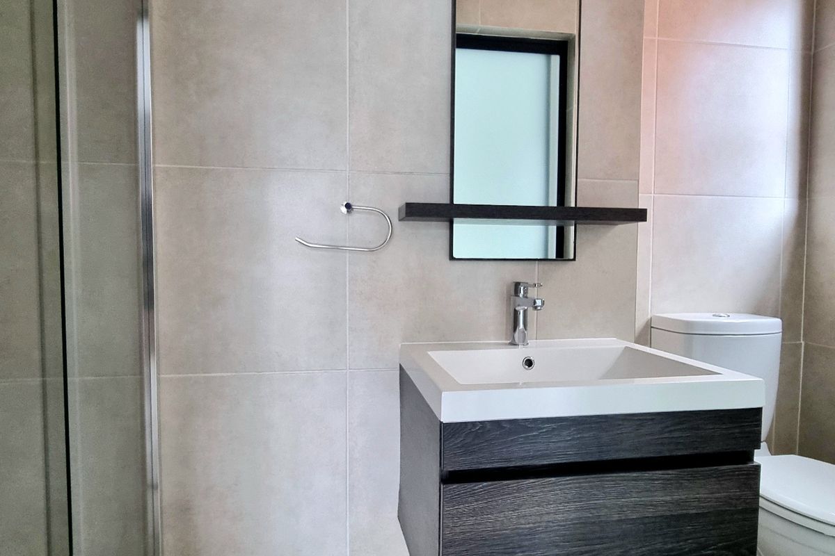 Modern bathroom featuring a floating vanity, basin with mixer tap, wall-mounted mirror, toilet, and a glass-enclosed shower with neutral wall tiling.