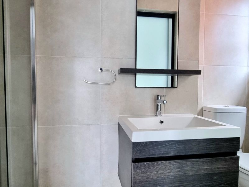 Modern bathroom featuring a floating vanity, basin with mixer tap, wall-mounted mirror, toilet, and a glass-enclosed shower with neutral wall tiling.