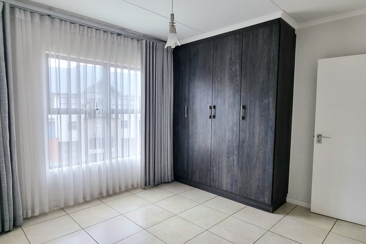 A bright, empty bedroom featuring neutral tiled flooring and dark wood-grain built-in cupboards, offering a clean and versatile space.