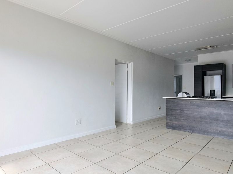 Spacious open-plan living area featuring tiled flooring and a modern kitchen with a central island, built-in cabinetry, and integrated cooking appliances.