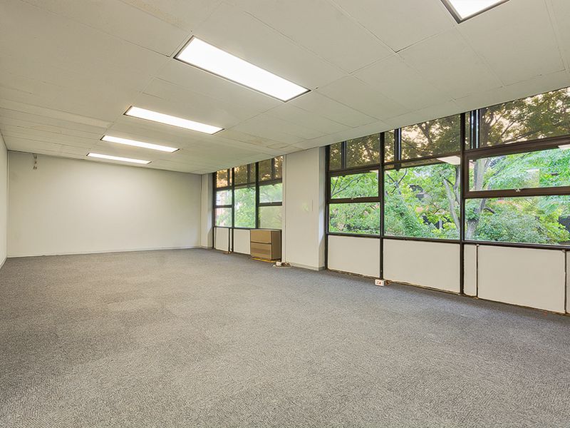 An empty, open-plan commercial office space featuring large windows with natural views, recessed lighting, and carpeted flooring.