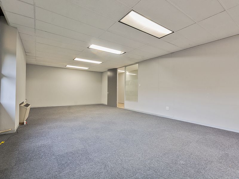 A vacant commercial office space featuring neutral carpeting, a suspended ceiling with recessed lighting, and a glass partition wall.