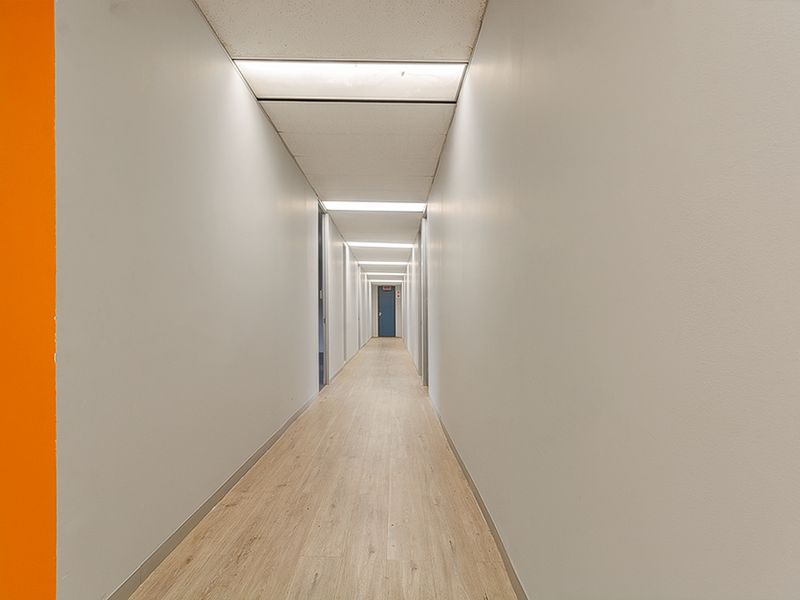A clean, well-lit commercial hallway featuring wood-look vinyl flooring, suspended acoustic ceiling tiles, and recessed lighting.